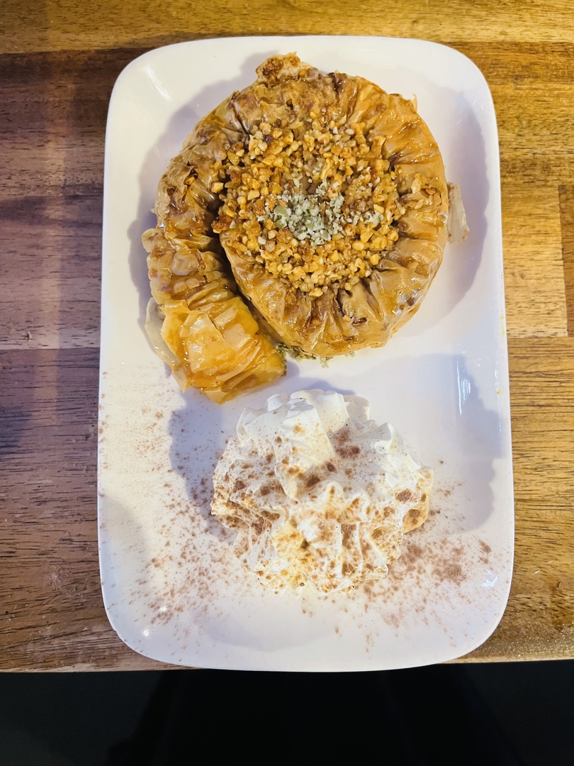 Freshly baked baklava — a golden coil topped with crushed pistachio beside a swirl of cinnamon cream