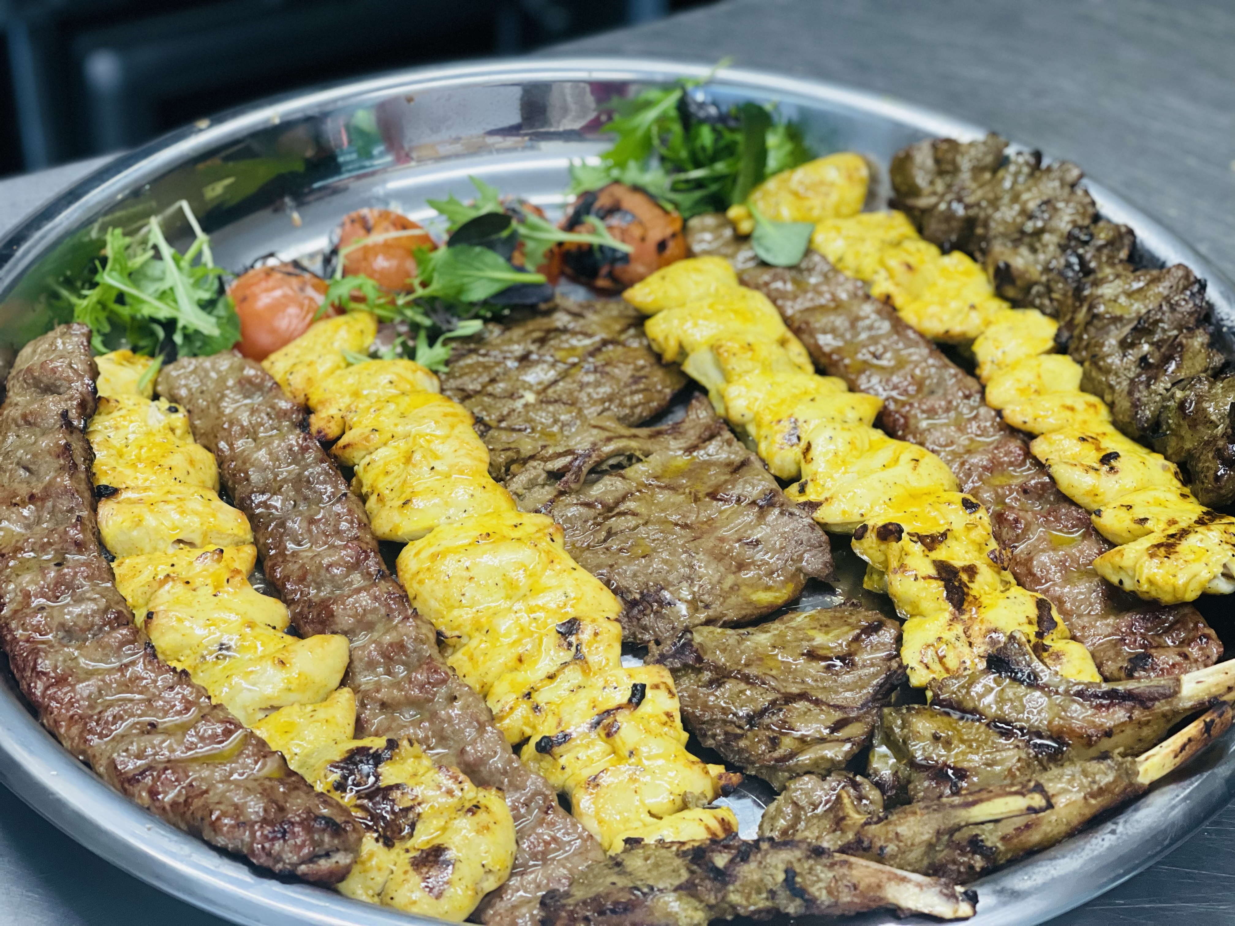 A silver tray of mixed charcoal kebabs at Akdeniz — koobideh, barg and saffron joojeh chicken skewers with herb salad