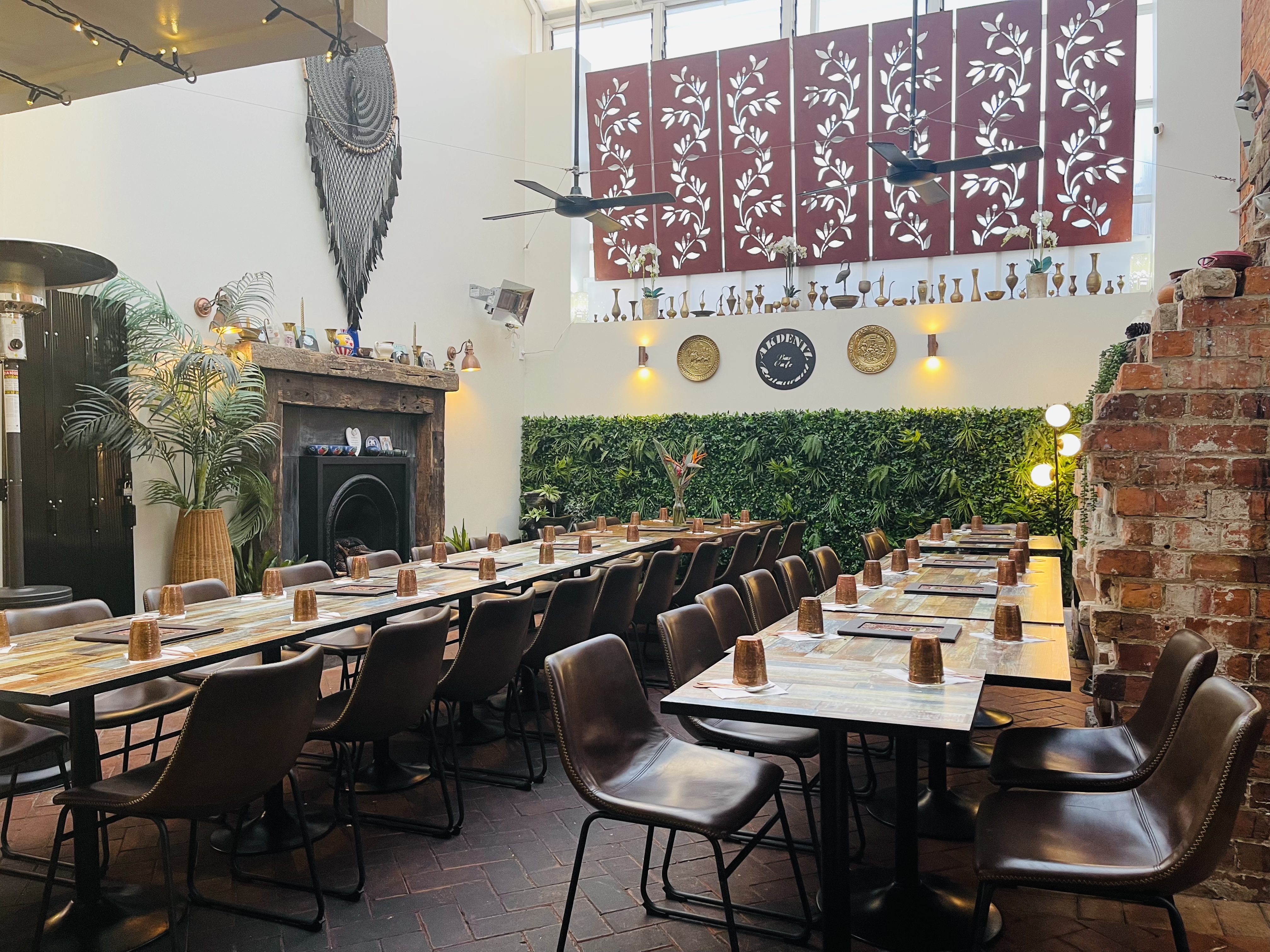 The main dining room at Akdeniz in Devonport — marble-topped tables, leather chairs, exposed red brick, a living green wall and the round AKDENIZ signboard